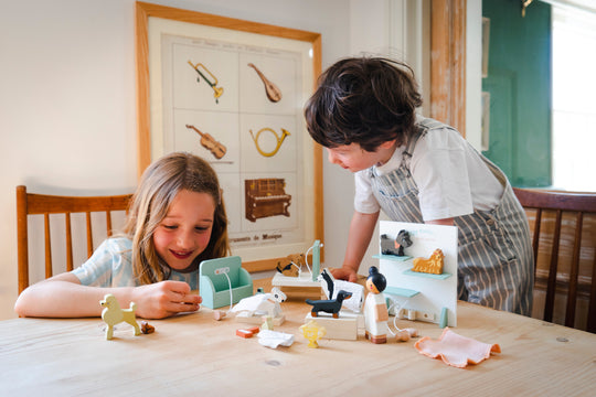 Two children playing with toys at a table in a room with a decorative wall poster.