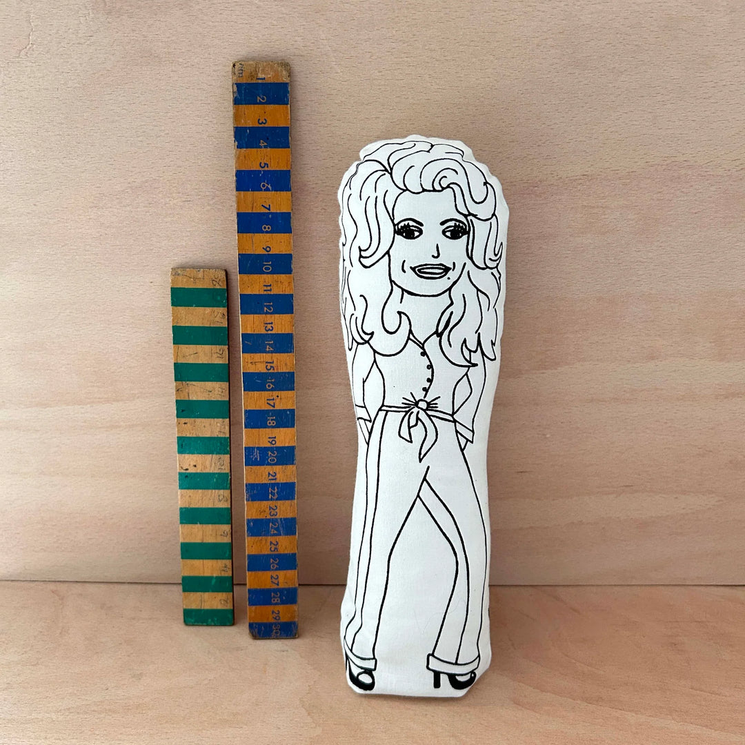 Wooden measuring stick with colourful stripes next to a white plush toy with a black outline of a person on a wooden surface.