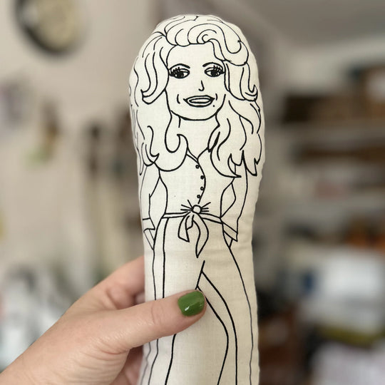 Hand holding a plush toy with a black and white outline of a person on a beige background.