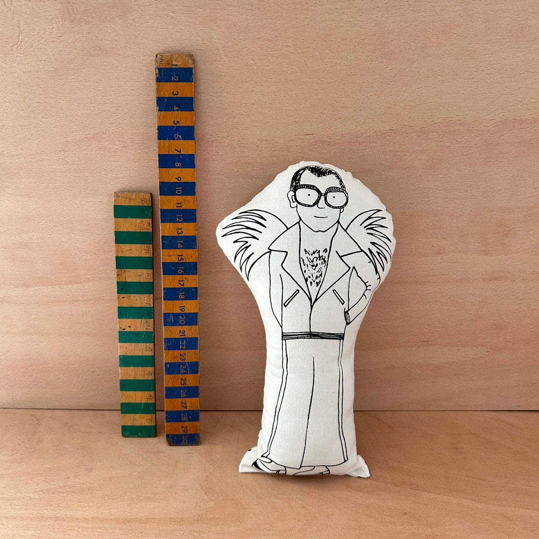 Decorative doll with a black and white illustration of a person, standing next to two wooden rulers on a wooden surface.