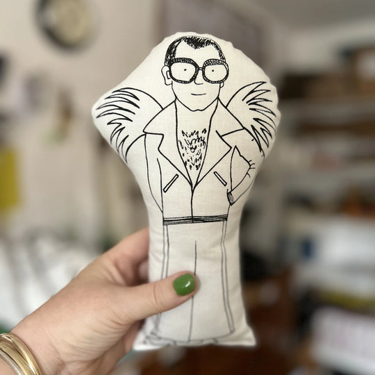 Hand holding the doll with a black and white illustration of a person wearing glasses and a suit.
