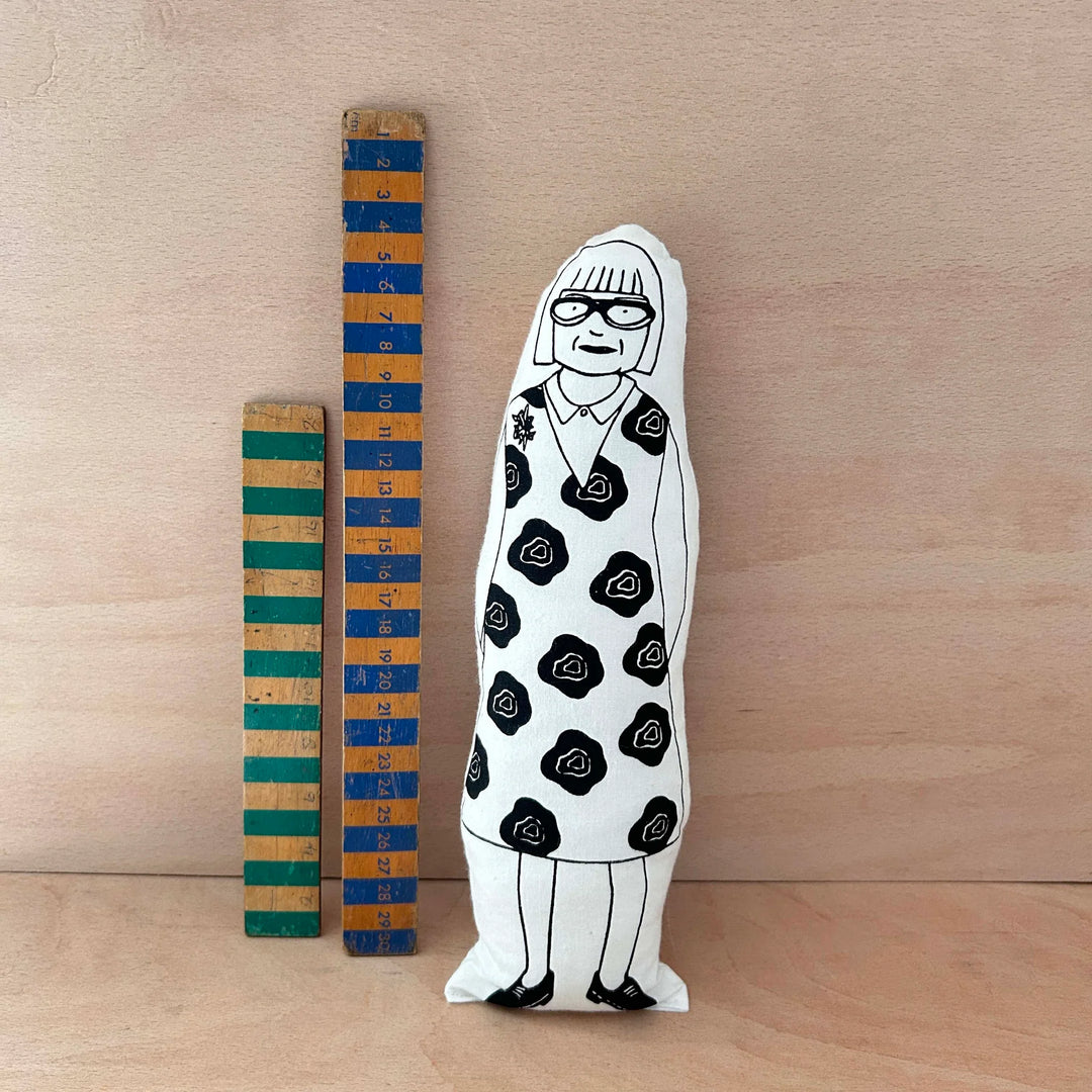 Screen printed doll cushion of Esme Young next to two wooden rulers against a wooden background