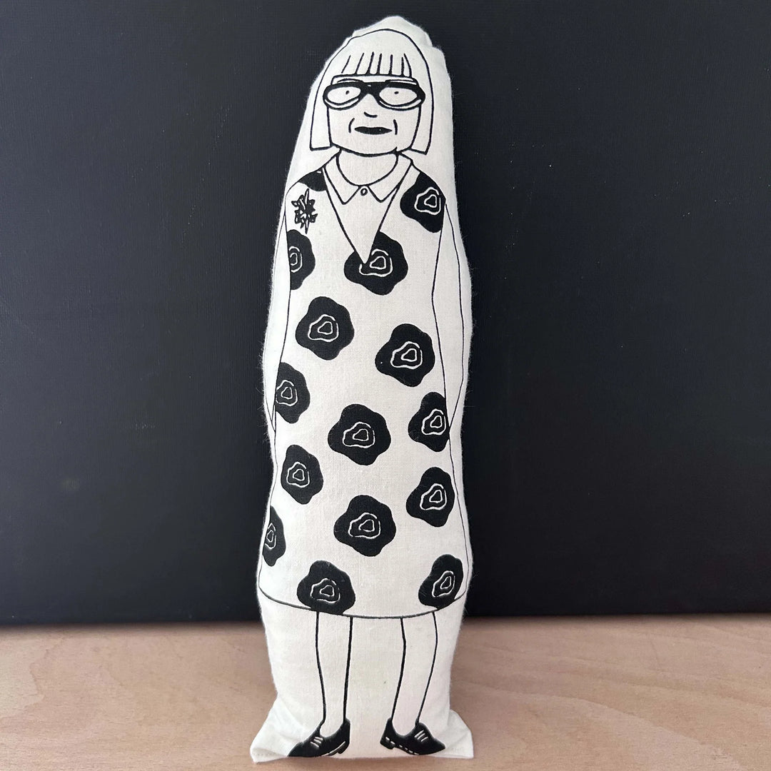 Screen printed doll cushion with white fabric and black illustration depicting TV-presenter and fashion designer Esme Young, wearing a bold floral dress and statement glasses