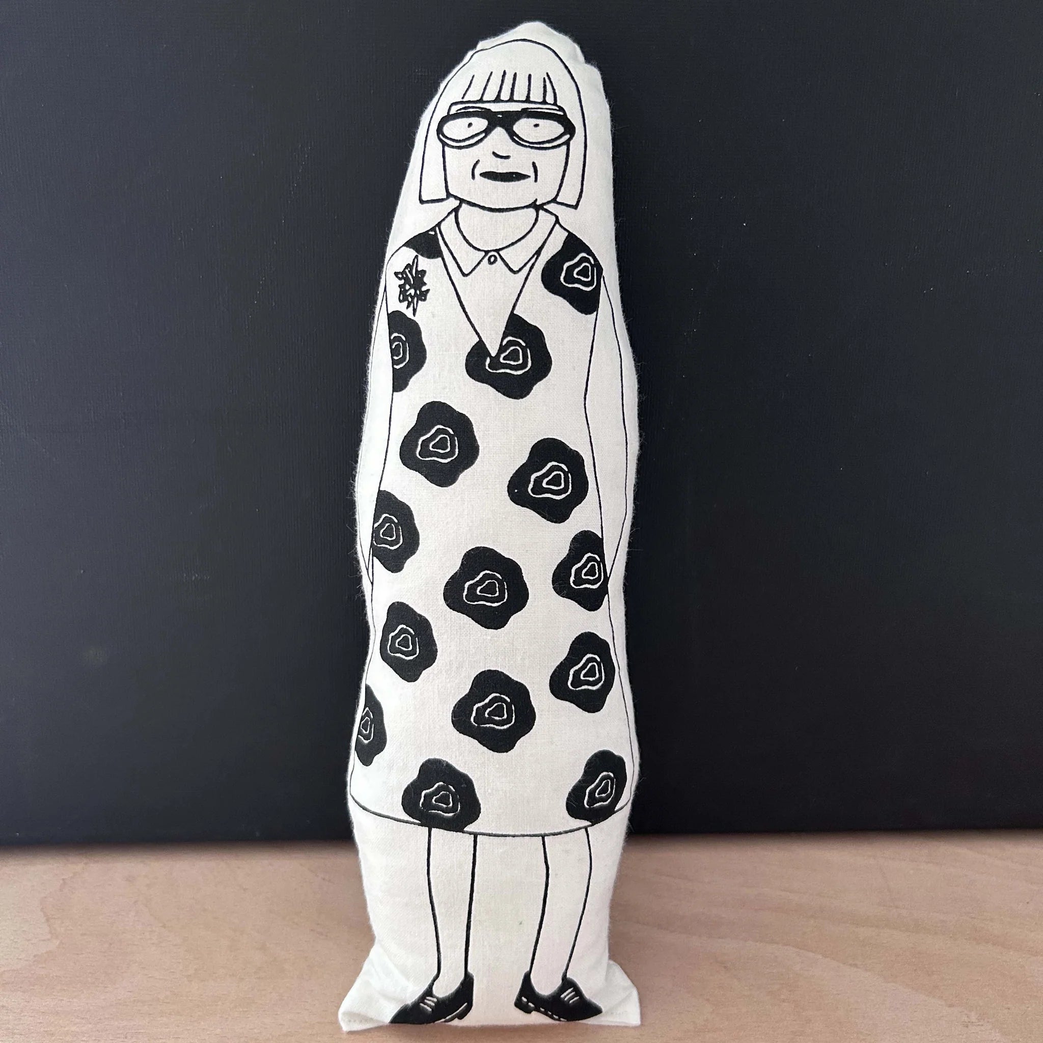 Screen printed doll cushion with white fabric and black illustration depicting TV-presenter and fashion designer Esme Young, wearing a bold floral dress and statement glasses
