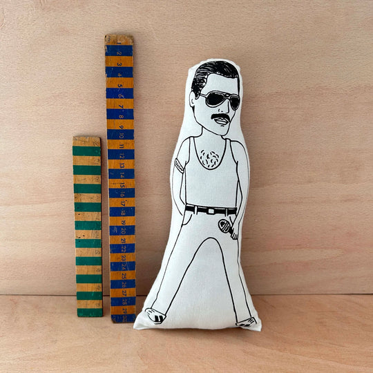 Screen printed doll cushion of Freddie Mercury next to two wooden rulers on a wooden background