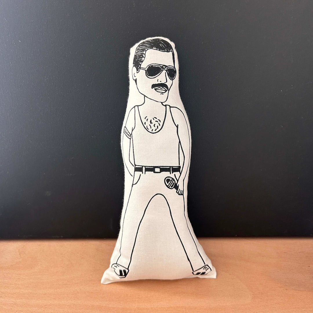 Screen printed doll cushion with white fabric and black illustration depicting the singer Freddie Mercury, wearing dark sunglasses, holding a microphone with his legs wide and wearing a tank top