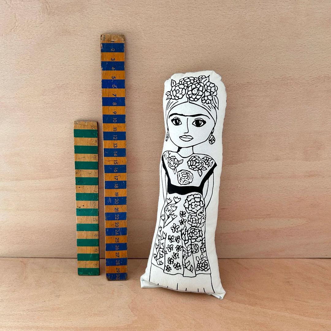 Screen printed doll cushion of Frida Kahlo next to two wooden rulers on a wooden background