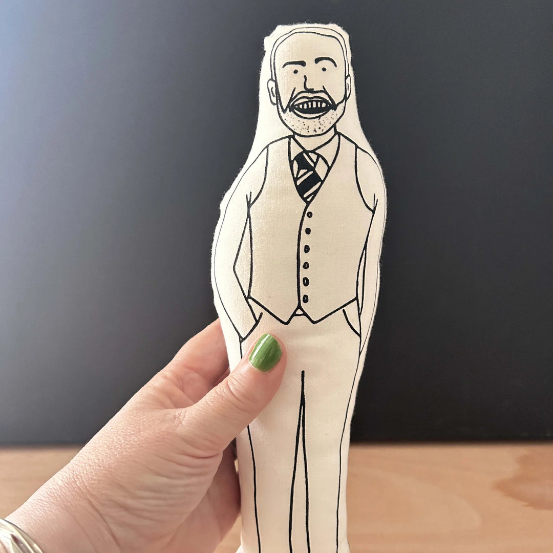 Hand holding a screen printed doll cushion with white fabric and black illustration depicting football manager  Gareth Southgate wearing his classic waistcoat with his hands in his pockets