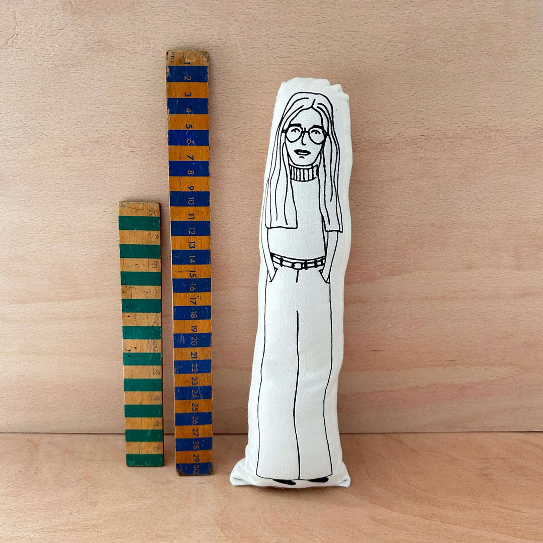 Screen printed doll cushion ofGloria Steinem next to two wooden rulers against a wooden background