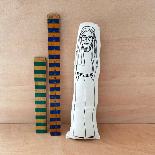 Screen printed doll cushion ofGloria Steinem next to two wooden rulers against a wooden background