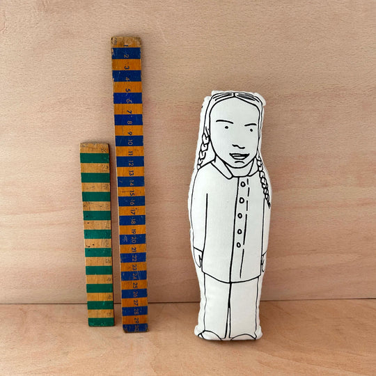 Screen printed doll cushion of Greta Thunberg next to two wooden rulers on a wooden background