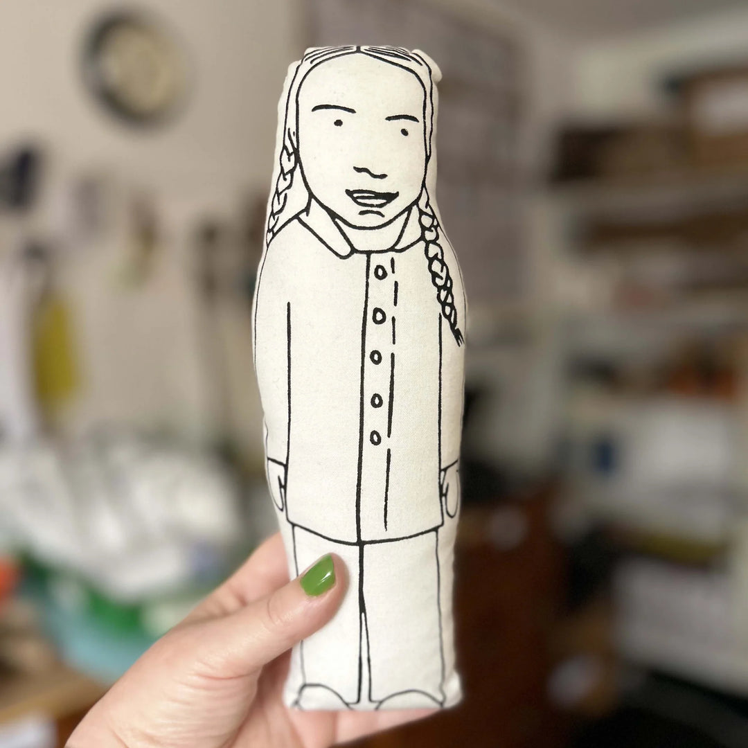 Hand holding up screen printed doll cushion of Greta Thunberg with a blurred background
