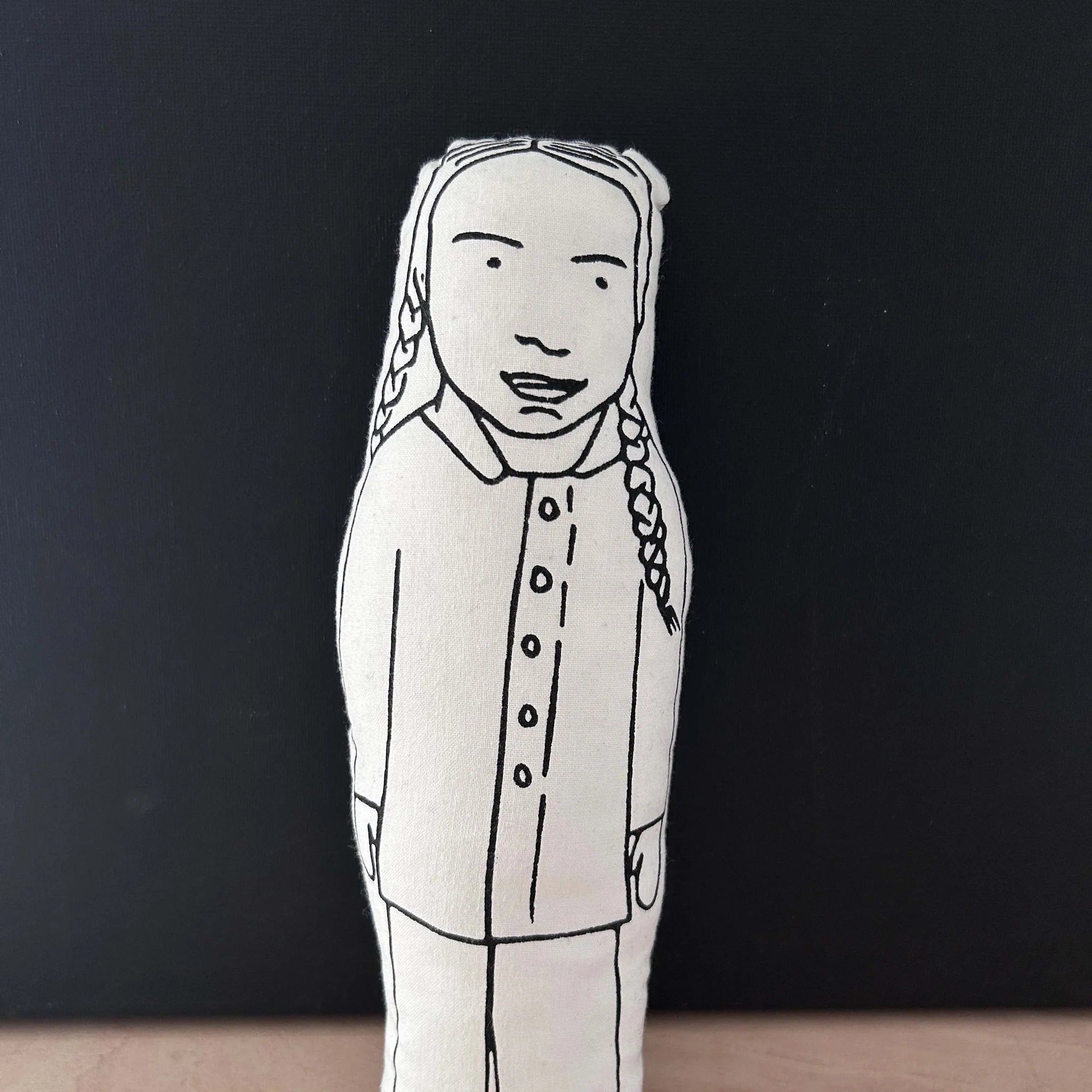 Screen printed doll cushion with white fabric and black illustration depicting a cartoon image of climate activist Great Thunberg