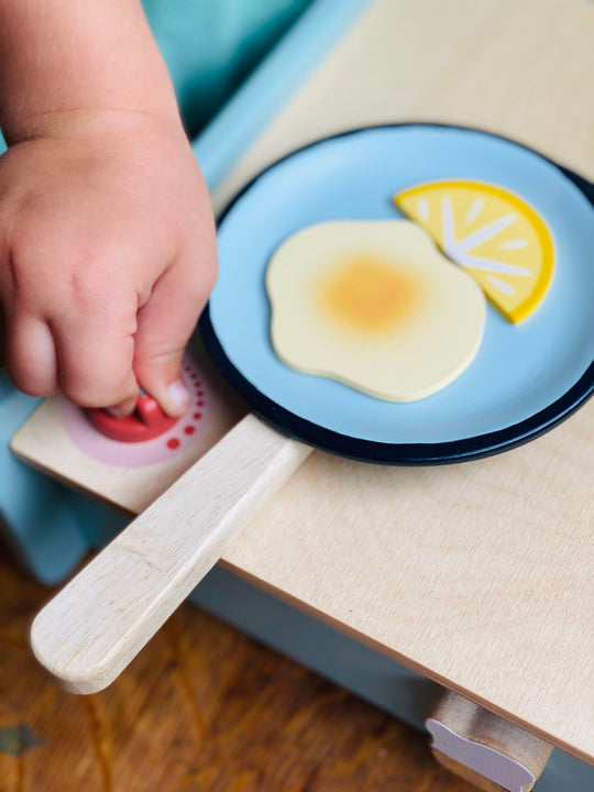 Child's hand interacting with a toy kitchen set on a wooden surface.