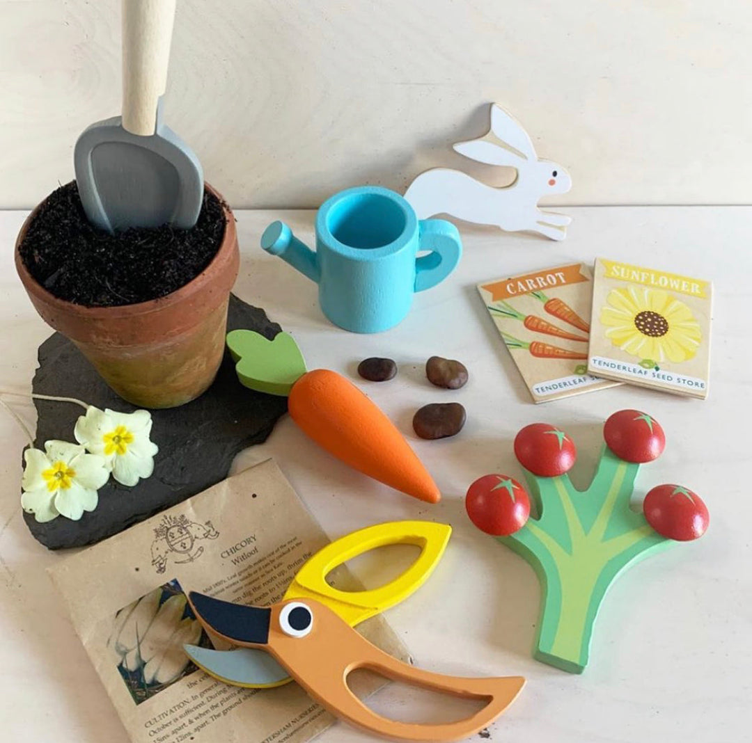 Set of colourful children's gardening toys including a pot, tools, and seed packets on a light surface.