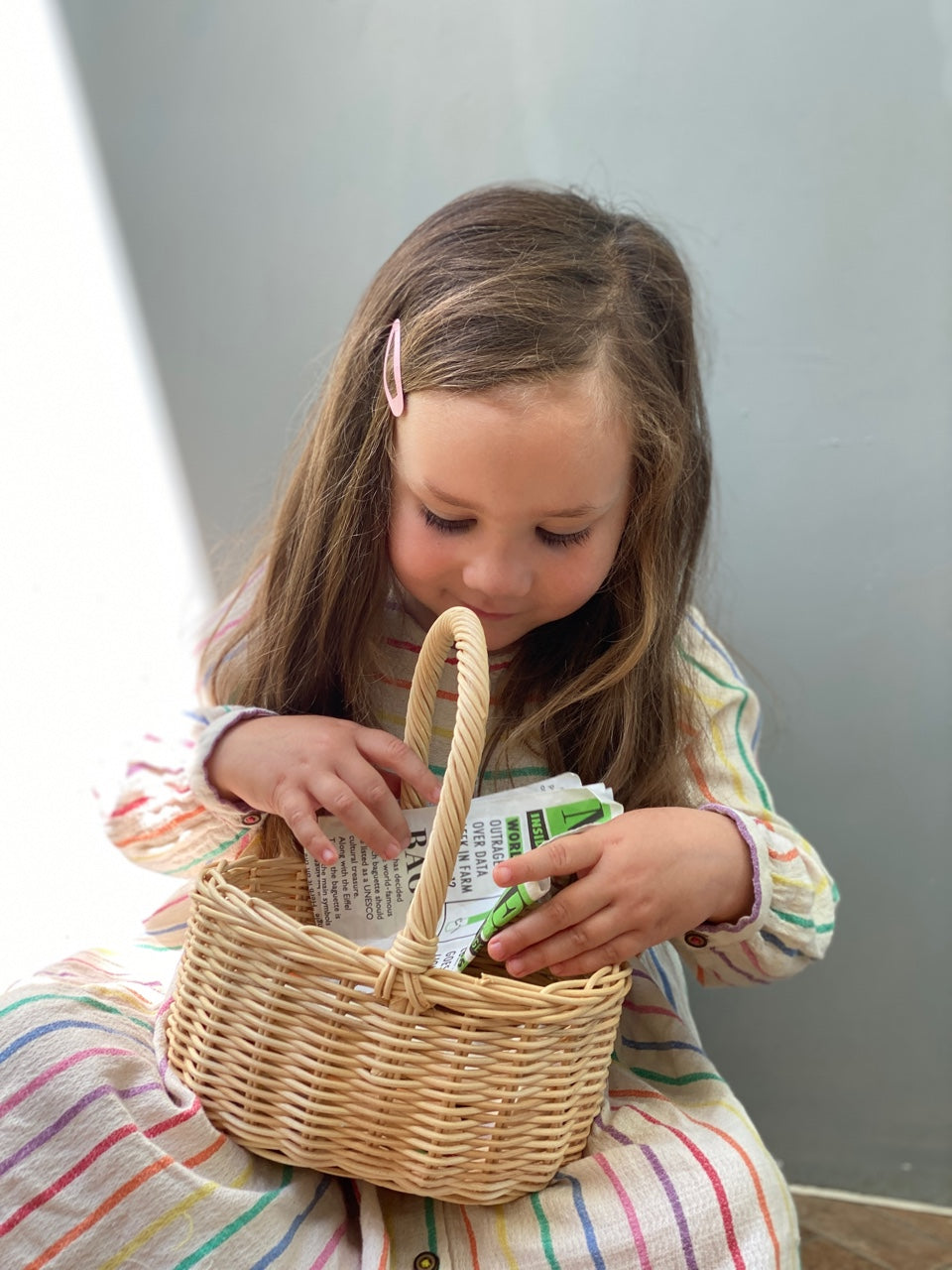 Child in a striped dress sitting on the floor with a wicker basket.