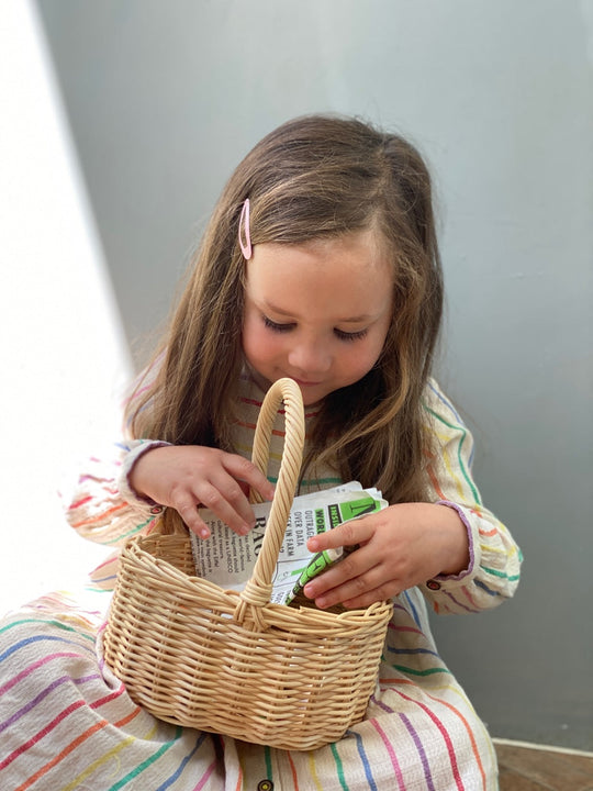 Child in a striped dress sitting on the floor with a wicker basket.