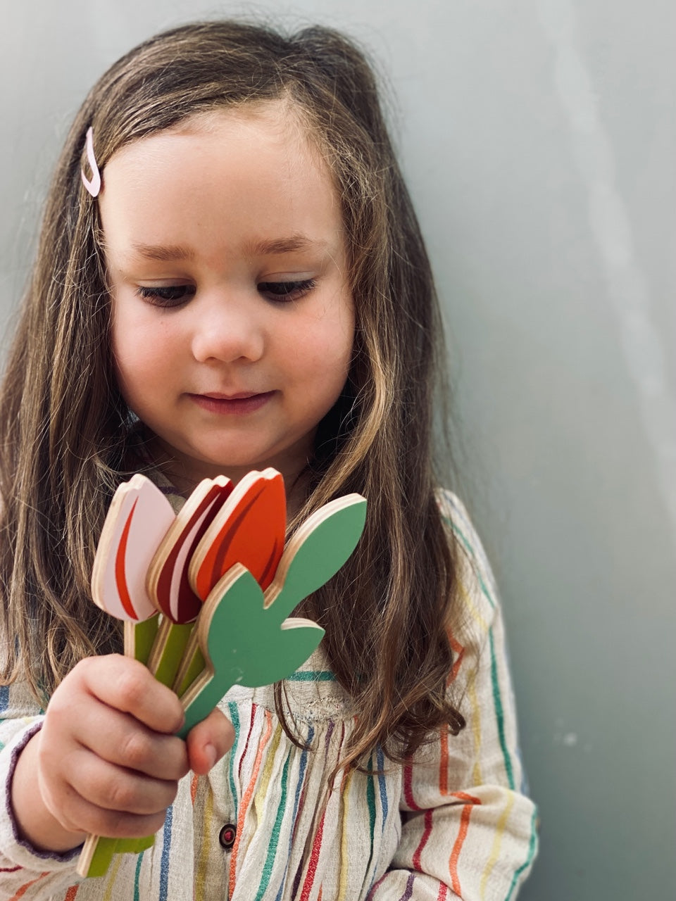 Child holding a set of colourful wooden tulips against a plain background