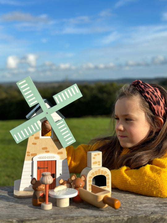 Child playing with a wooden windmill toy set outdoors on a sunny day.