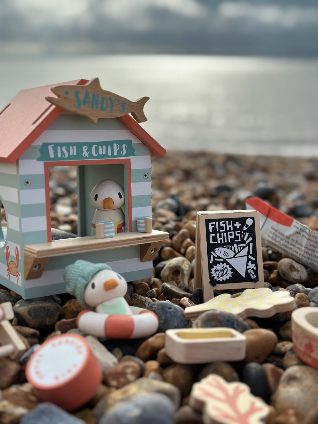 Miniature toy fish and chip shop on a pebble beach with ocean in the background