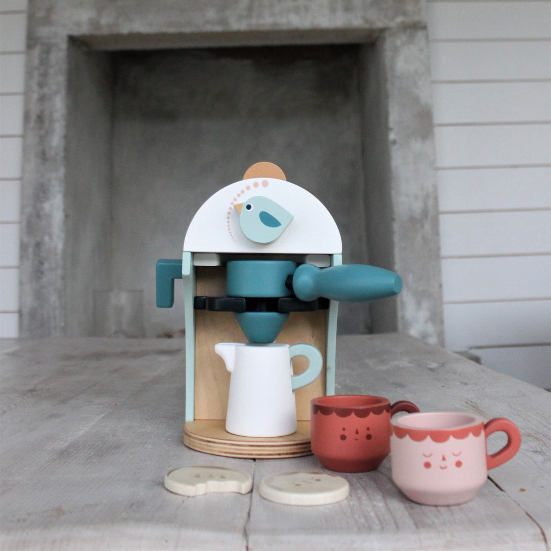 Children's toy coffee maker set with cups and a bird design on a wooden surface.