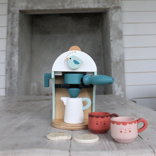 Children's toy coffee maker set with cups and a bird design on a wooden surface.