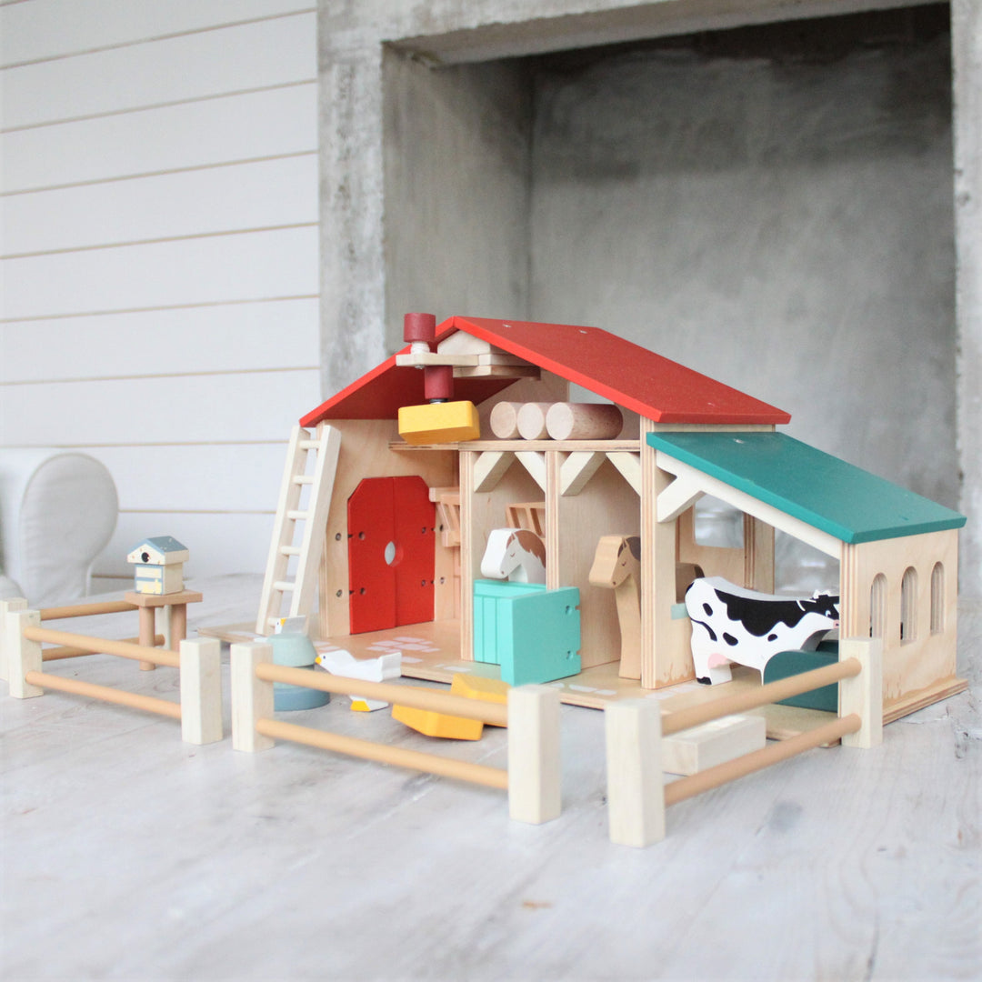 Colorful wooden toy barn with animals on a concrete floor.