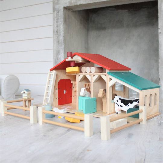 Colorful wooden toy barn with animals on a concrete floor.