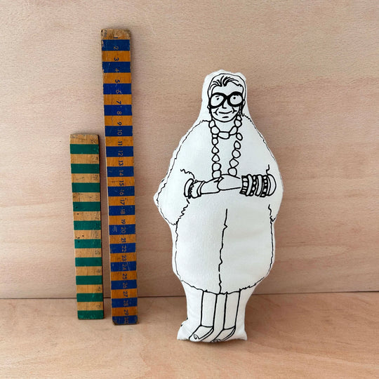 Screen printed doll cushion of Iris Apfel next to two wooden rulers on a wooden background