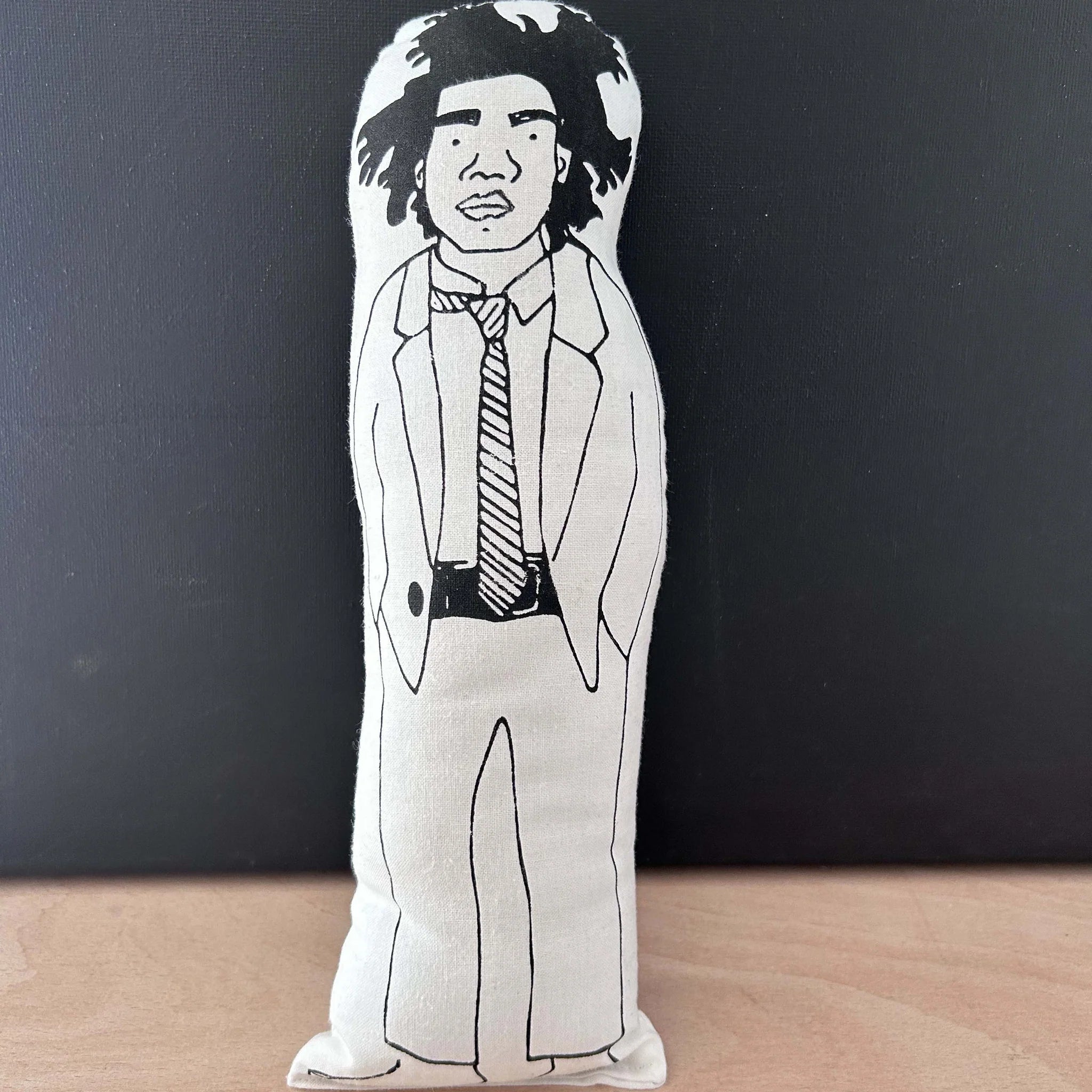 Screen printed doll cushion with white fabric and black illustration depicting artist Jean Michel Basquiat wearing a casual suit with his hands in his pockets