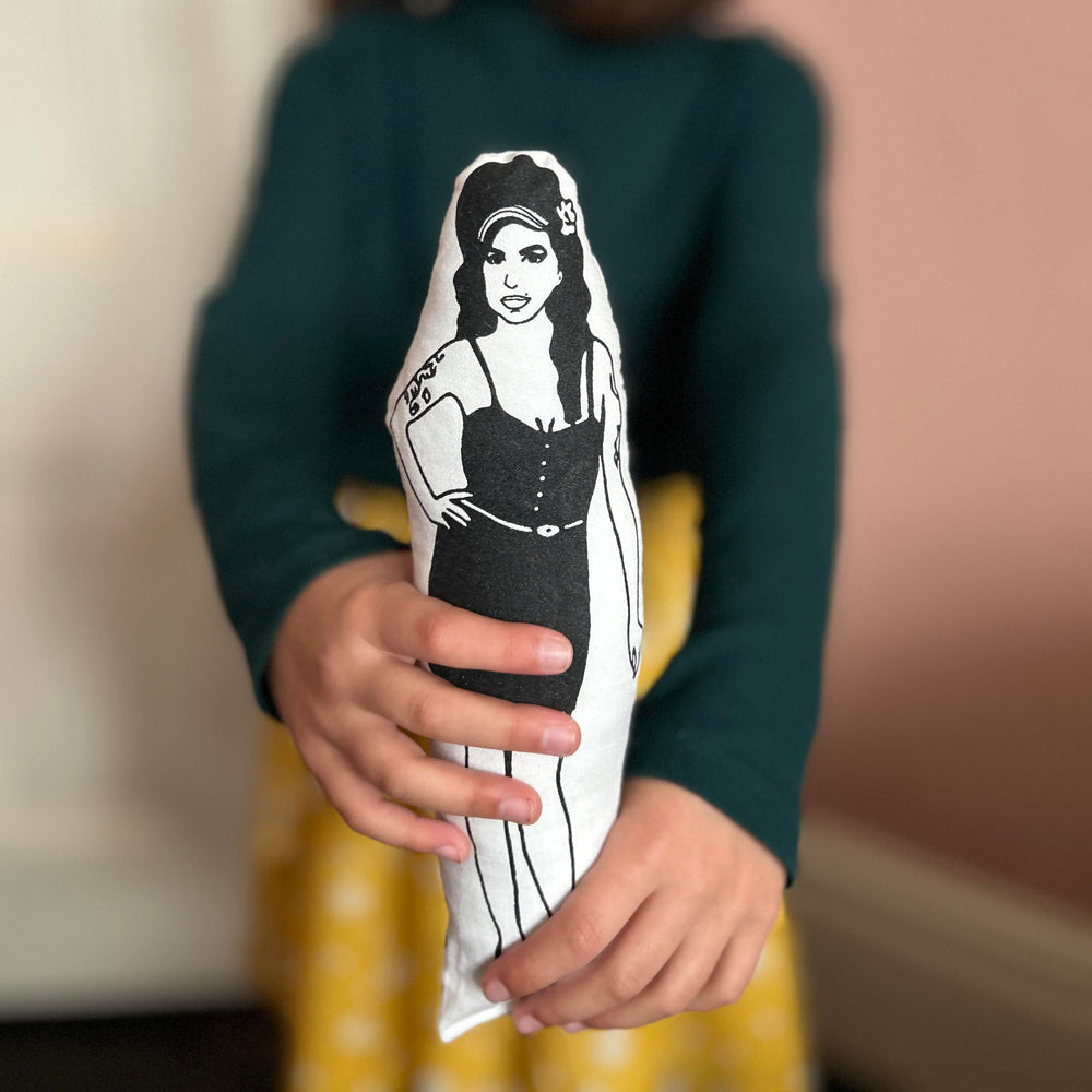 A child holding out a screen printed cushion doll of Amy Winehouse with a black and white design.
