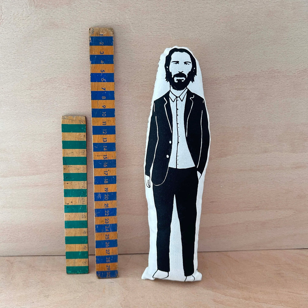 Screen printed doll cushion of Keanu Reeves next to two wooden rulers on a wooden background