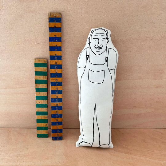 Screen printed doll cushion of Keith Brymer Jones next to two wooden rulers against a wooden background