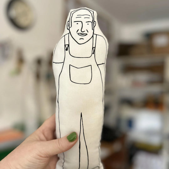 A hand holding screen printed doll cushion of Keith Brymer Jones with a blurred background