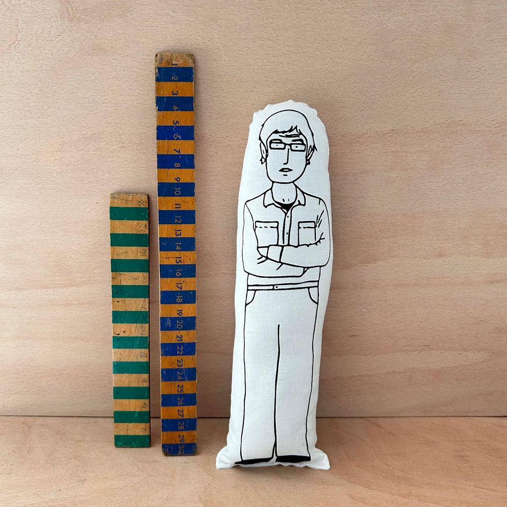 Screen printed doll cushion of Louis Therous next to two wooden rulers against a wooden background