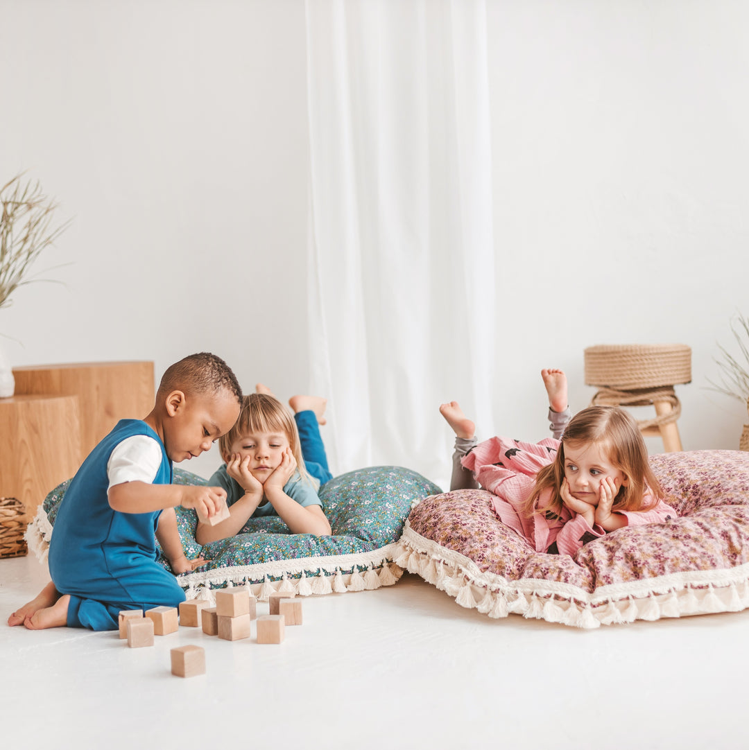 Children playing on cushions in a bright room with white walls and a wooden stool.