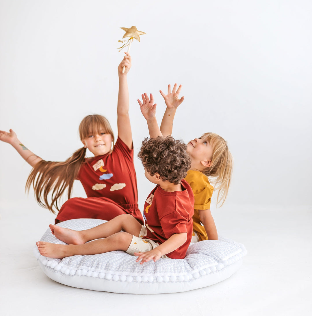Three children playing on a light grey floor cushion with a plain background