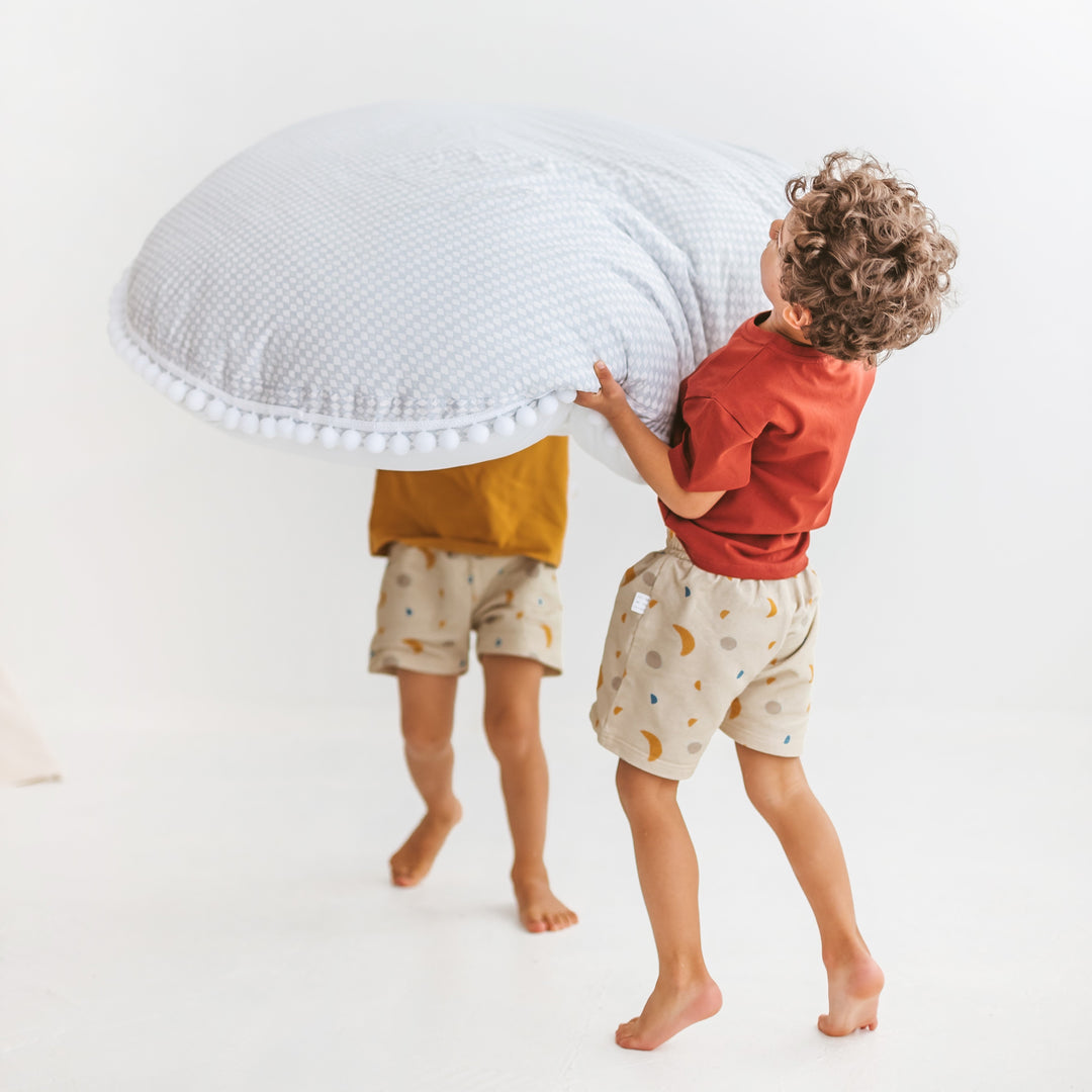 Two children playing with a large round pillow on a white background