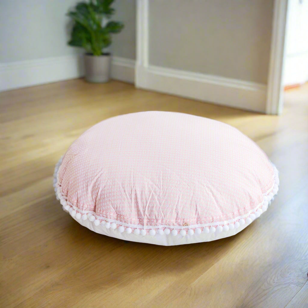 Round floor cushion in light pink with a subtle diamond pattern with white pom pom trim