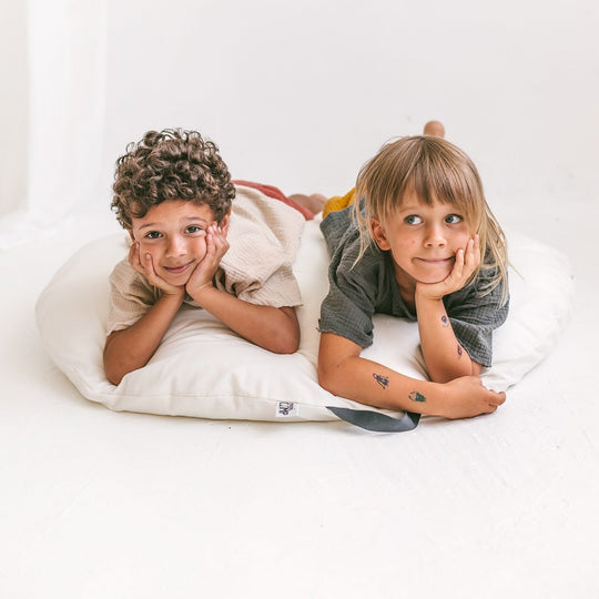 Two children lying on a white pillow with a plain background