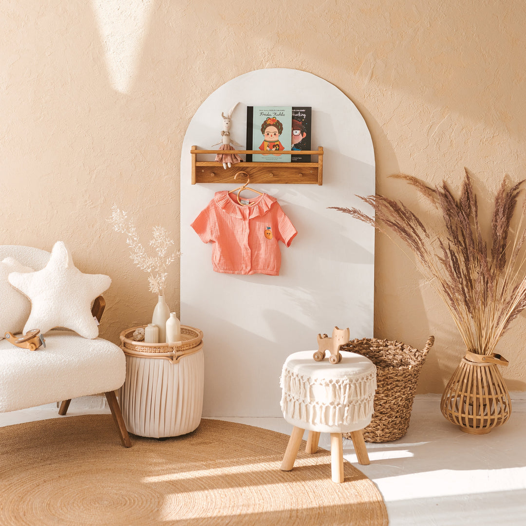 Children's room with a white arched shelf, pink shirt, and decorative items against a beige wall.