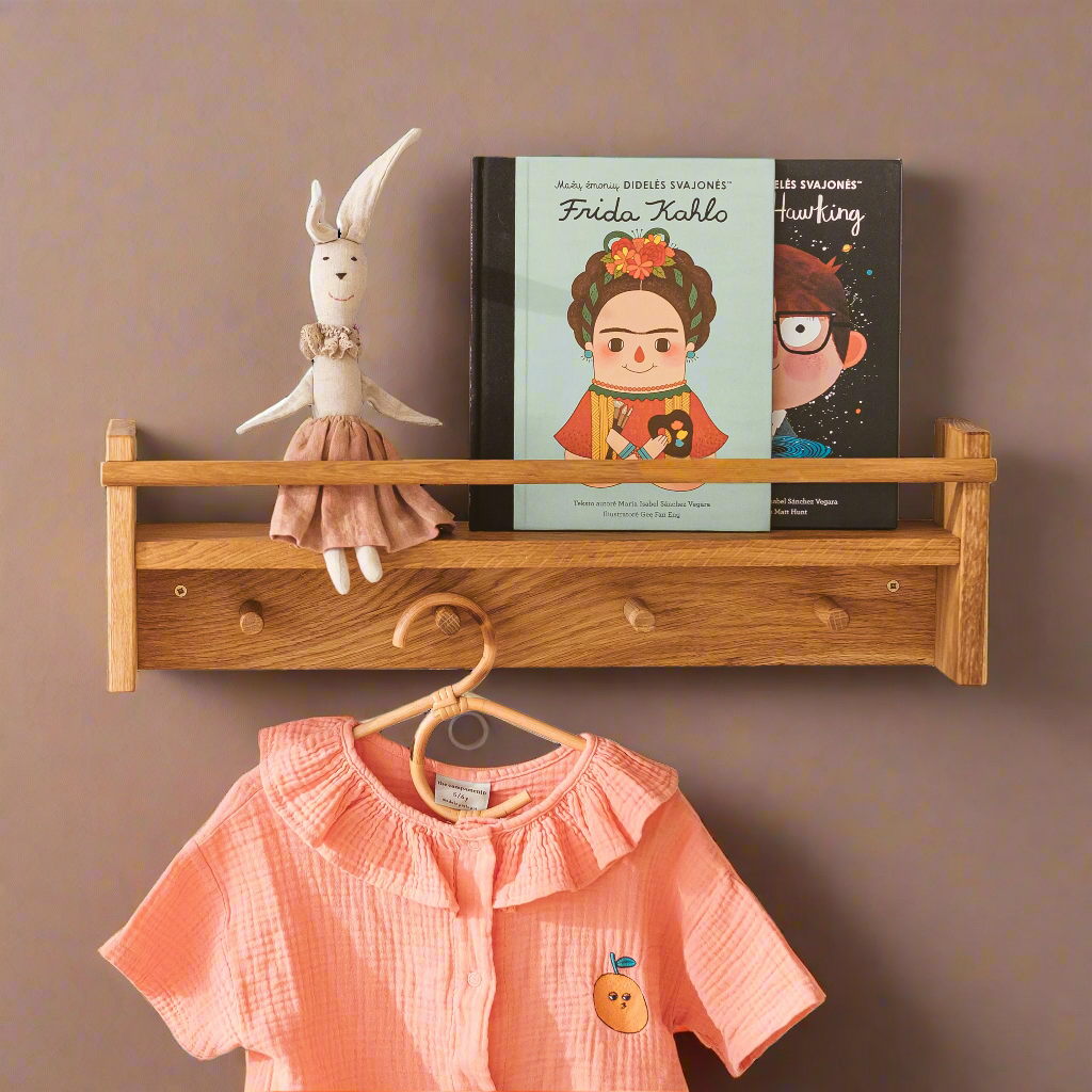 Wooden shelf with books and a doll with wooden pegs and a pink shirt on a hanger hanging off one of the wooden pegs