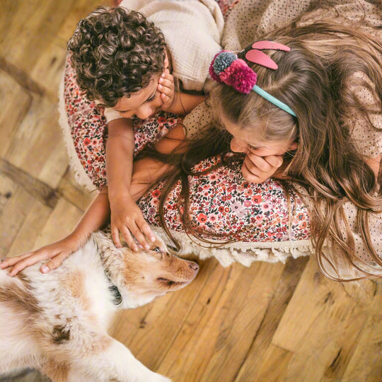 Two children playing with a dog while lying on floral floor cushion