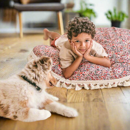 Child lying on a floral cushion with his face in his hands with a dog next to him