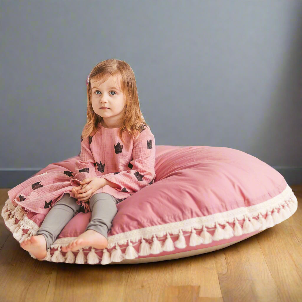 Child sitting on a large pink cushion with tassels