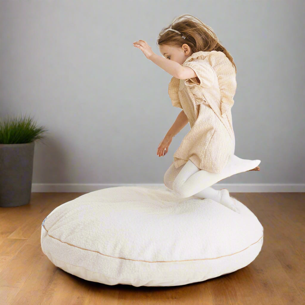 Child jumping onto large pale beige floor cushion