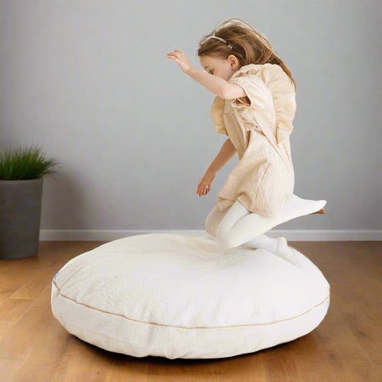 Child jumping onto large pale beige floor cushion