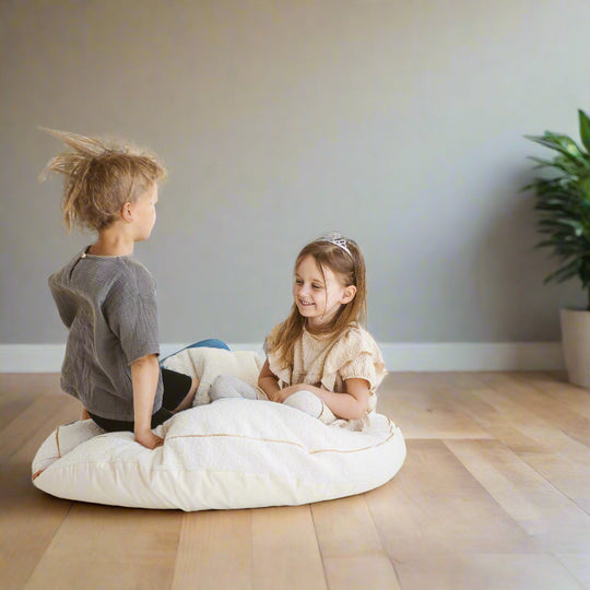 Two children sitting on a large pale beige floor cushion