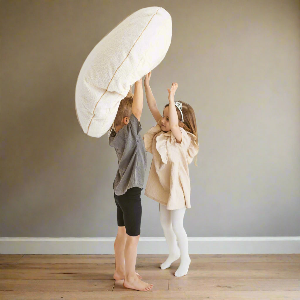 Two children playing with a pale beige pillow