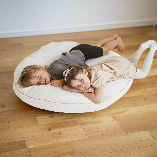 Two children lying on a large circular pale beige floor cushion